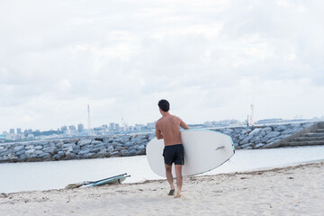 Asian man holding surf board on the beach at morning