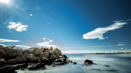 Paisaje del mar con unas rocas delante y rayos de sol entrando por una esquina