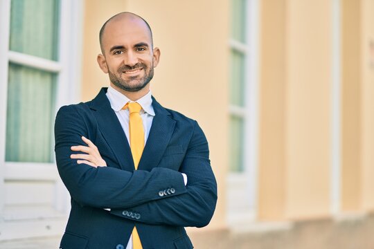 Young hispanic bald businessman with arms crossed smiling happy at the city.