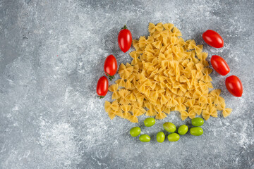Uncooked farfalle and tomatoes on marble background