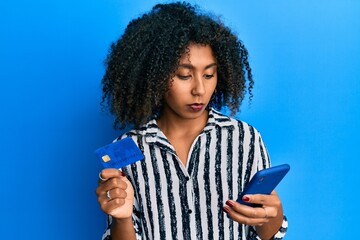 Beautiful african american woman with afro hair holding smartphone and credit card relaxed with serious expression on face. simple and natural looking at the camera.