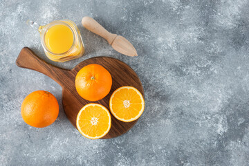 A glass pitcher of juice with fresh orange fruits on stone background