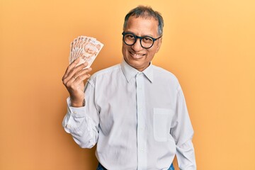 Middle age indian man holding 50 turkish lira banknotes looking positive and happy standing and...