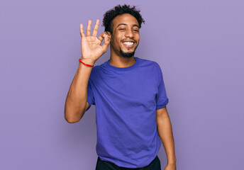 Fototapeta premium Young african american man with beard wearing casual purple t shirt smiling positive doing ok sign with hand and fingers. successful expression.