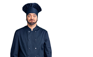 Young hispanic man wearing cooker uniform puffing cheeks with funny face. mouth inflated with air,...