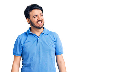 Fototapeta premium Young hispanic man wearing casual clothes looking away to side with smile on face, natural expression. laughing confident.
