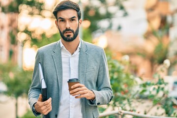 Young hispanic businessman smiling happy drinking take away coffee at the city.
