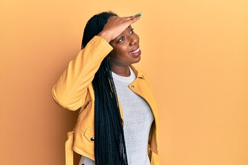 Young african american woman wearing casual jacket very happy and smiling looking far away with hand over head. searching concept.