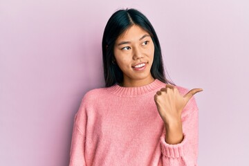 Young chinese woman wearing casual clothes pointing thumb up to the side smiling happy with open mouth