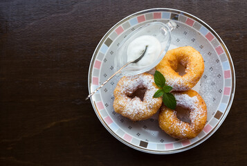 Donuts on the plate. Three donuts with powdered sugar, mint leaf and sour cream on the plate. Dark wooden background.