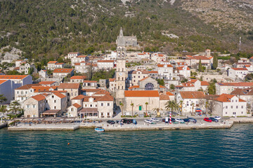 Fototapeta na wymiar Aerial shot of the old coastal town of Perast at the foot of the mountain. Seaside promenade, residential buildings with traditional balkan red roofs, ancient Cathedral and coastline