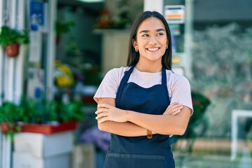 Young latin shopkeeper girl with arms crossed smiling happy standing at the florist