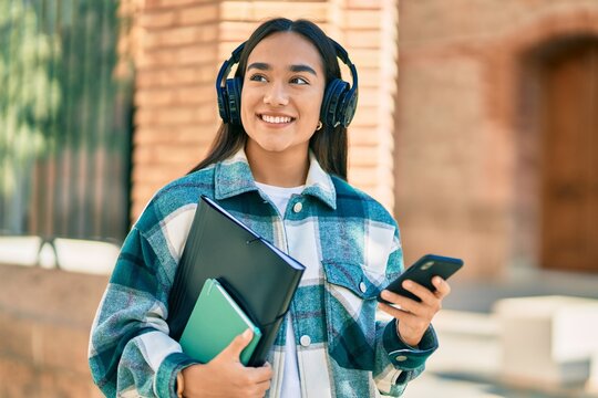 Young latin student girl smiling happy using smartphone and headphones at the city.