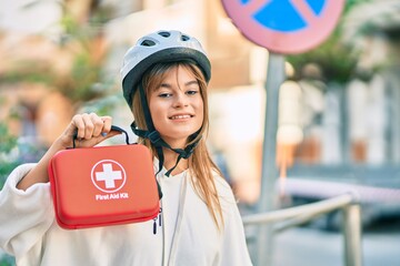 Caucasian sporty teenager girl wearing bike helmet holding first aid kit at the city.