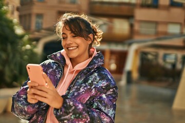 Young hispanic sporty woman smiling happy using smartphone at the city.