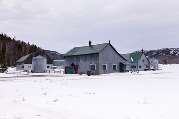 Fototapeta na wymiar Late winter landscape with grey farm buildings seen during a cloudy day, St-André-de-Kamouraska, Quebec, Canada
