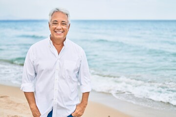 Handosme hispanic man with grey hair smiling happy at the beach, enjoying holidays on summer