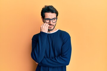 Obraz premium Young hispanic man wearing casual clothes and glasses looking stressed and nervous with hands on mouth biting nails. anxiety problem.