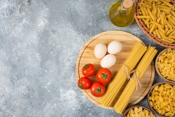 Variety of raw pasta with eggs, fresh tomatoes and bottle of oil