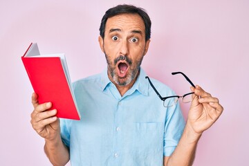 Middle age hispanic man reading book holding glasses afraid and shocked with surprise and amazed...