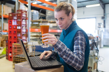 brewery worker at laptop inspecting glass of beer