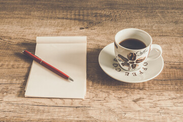 A notebook with a pen and a cup of coffee on a wooden rustic table