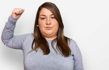 Beautiful brunette plus size woman wearing casual clothes strong person showing arm muscle, confident and proud of power