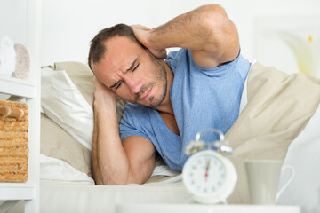 man in bed covering his ears as the alarm sounds