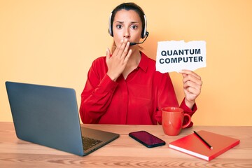 Young brunette woman holding quantum computer banner covering mouth with hand, shocked and afraid...