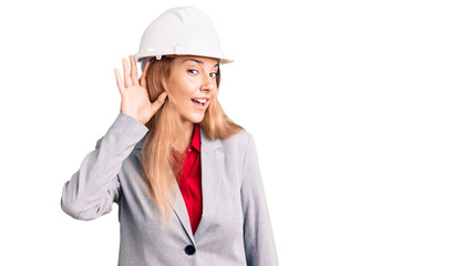 Beautiful young woman wearing architect hardhat smiling with hand over ear listening an hearing to rumor or gossip. deafness concept.