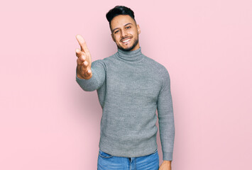 Young arab man wearing casual clothes smiling friendly offering handshake as greeting and welcoming. successful business.