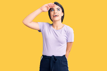 Brunette teenager girl wearing casual clothes very happy and smiling looking far away with hand over head. searching concept.