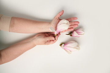 close-up of middle-aged woman's hand holding buds of spring flowers, pink magnolia, concept of awakening nature, aroma of plants, anti-aging cosmetology and care for aging skin