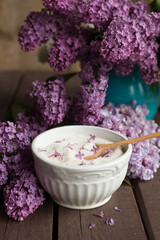 Purple lilac flower sugar in white bowl on dark wooden background with bunch of fresh flowers, homemade sugar with lilac flowers, centered, wooden spoon