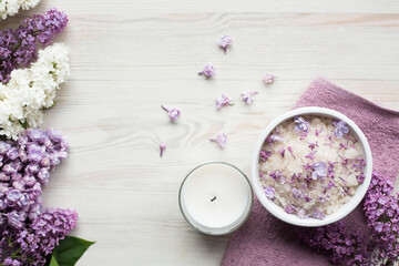 Homemade bath salt with fresh spring lilac flowers, home healthy spa, white candle for relaxation, light wooden background, purple towel, top view from above, copy space for text