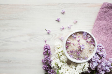 Obraz na płótnie Canvas Homemade bath salt with fresh spring lilac flowers, home healthy spa, relaxation, light wooden background, purple towel, top view from above, copy space for text