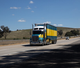 Fototapeta na wymiar Truck on a freeway with plane flying overhead in Australian Country Town midway between Sydney and Melbourne with nice blue sky and lush green trees as a backdrop