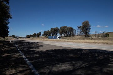 Truck on a freeway with plane flying overhead in Australian Country Town midway between Sydney and Melbourne with nice blue sky and lush green trees as a backdrop