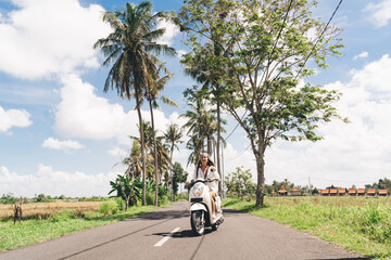 Cheerful young female biker riding scooter amidst palms on sunny day