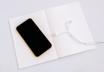 Mobile phone and headphone on white empty page