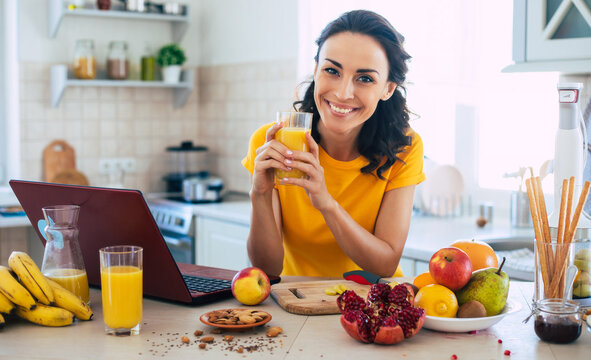 Cute beautiful and happy young brunette woman in the kitchen at home is preparing fruit vegan salad or a healthy smoothie and having fun