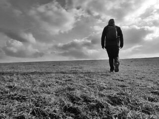 Fototapeta premium Black and white shot of a man walking across a field on a day of dramtic clouds in rural Franconia in northern Bavaria.