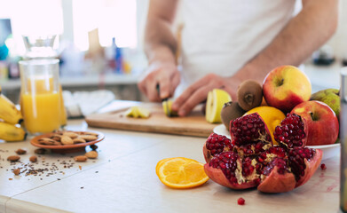 Handsome young sporty smiling man in the kitchen is preparing vegan healthy fruits salad and smoothie in a good mood