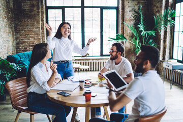 Cheerful young Asian woman presenting ideas to diverse coworkers in office