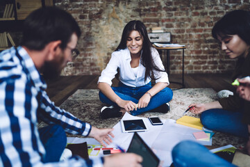 Fototapeta premium Group of happy male and female architects discussing blueprint details during collaborative meeting for friendly brainstorming in coworking space, dream team enjoying productive exam preparation