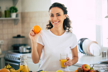 Cute beautiful and happy young brunette woman in the kitchen at home is preparing fruit vegan salad or a healthy smoothie and having fun