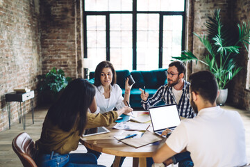 Group of young male and female coworkers collaborating on business project sitting at table with...