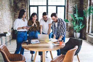 Group of diverse male and female coworkers checking received email message with news about startup investment, skilled hipster guys using laptop technology during collaborative meeting for studying