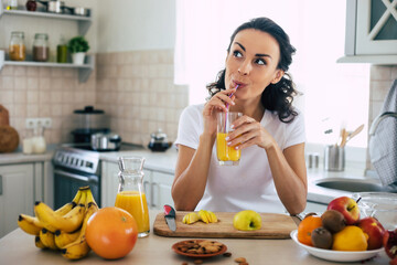 Cute beautiful and happy young brunette woman in the kitchen at home is preparing fruit vegan salad or a healthy smoothie and having fun