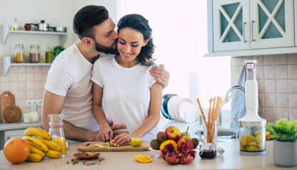 Excited happy beautiful young couple in love cooking in the kitchen and having fun together while making fresh healthy fruits salad